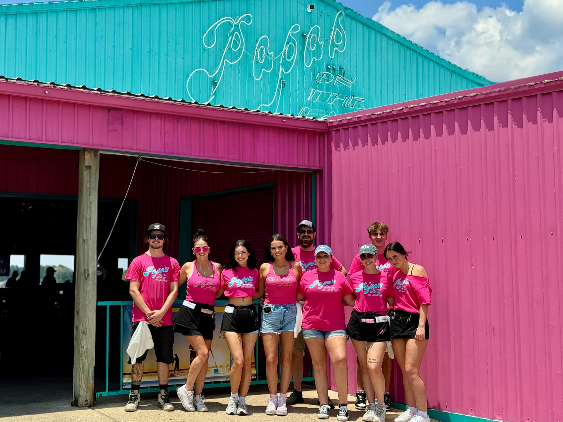 The Papa's crew in bright pink shirts lined up under the neon sign at the front entrance