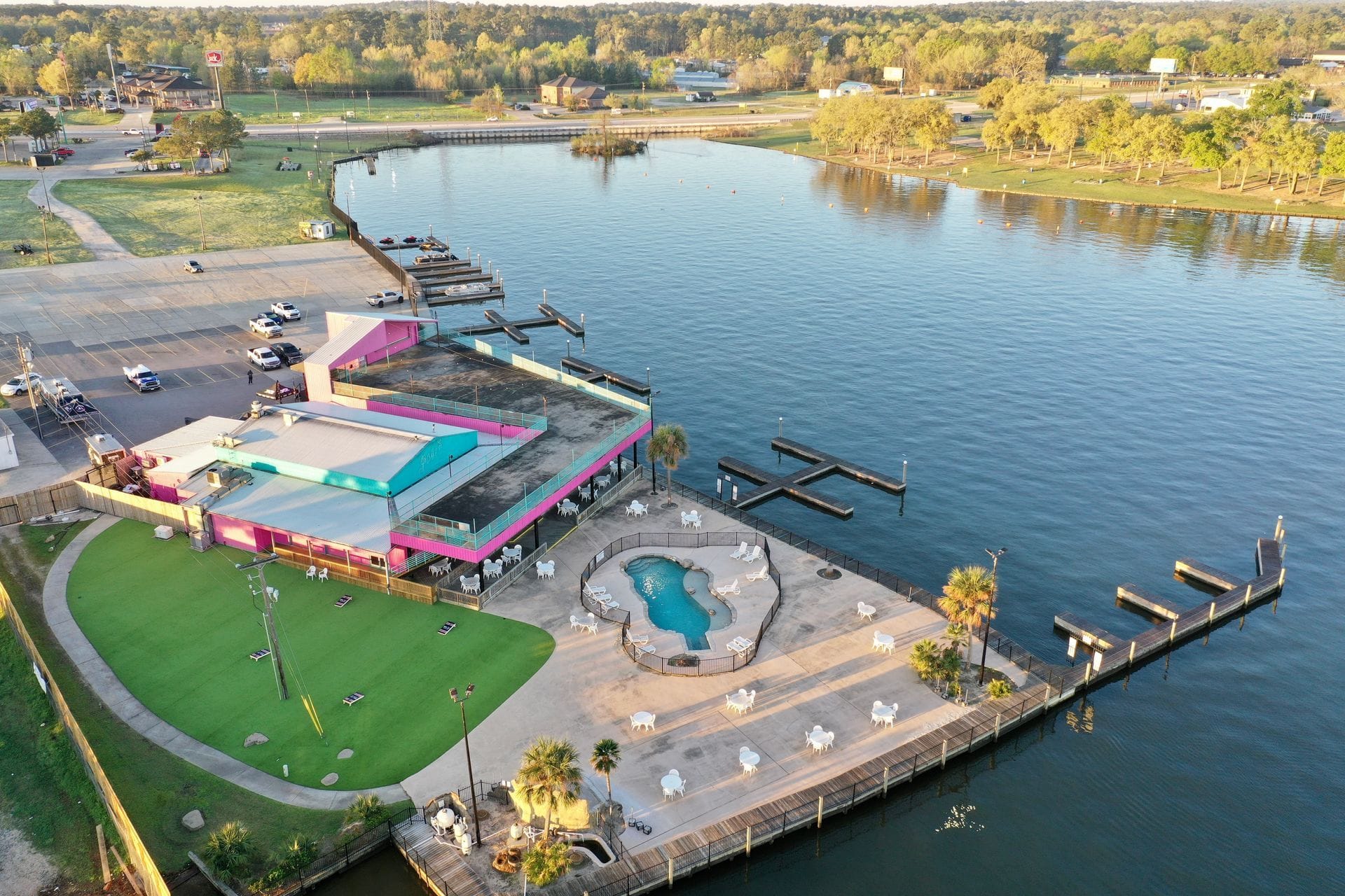 Aerial view of Papa's on the Lake — the bright pink lakeside grill, fenced pool deck, and boat docks on Lake Conroe