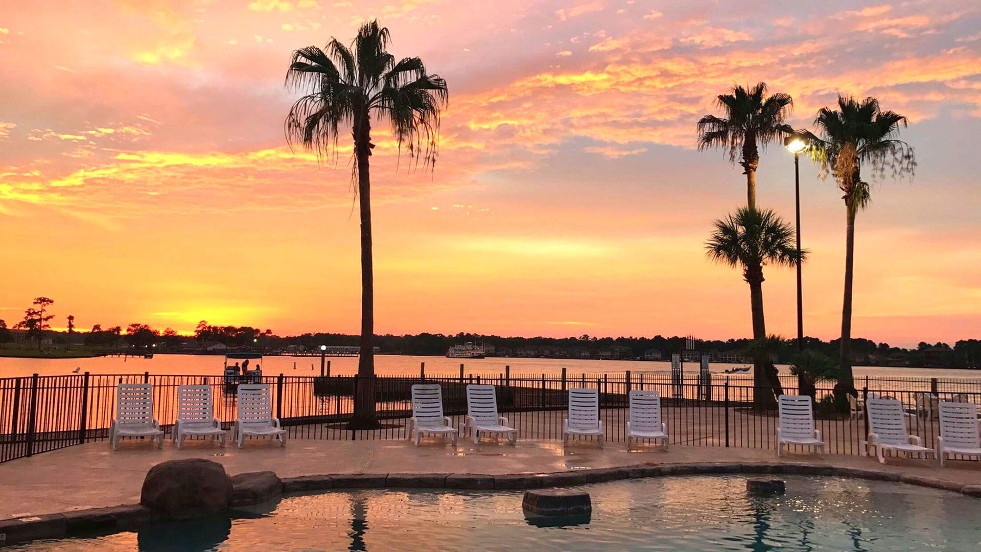 Papa's adults-only pool at sunset, palm trees and Lake Conroe glowing behind the lounge chairs